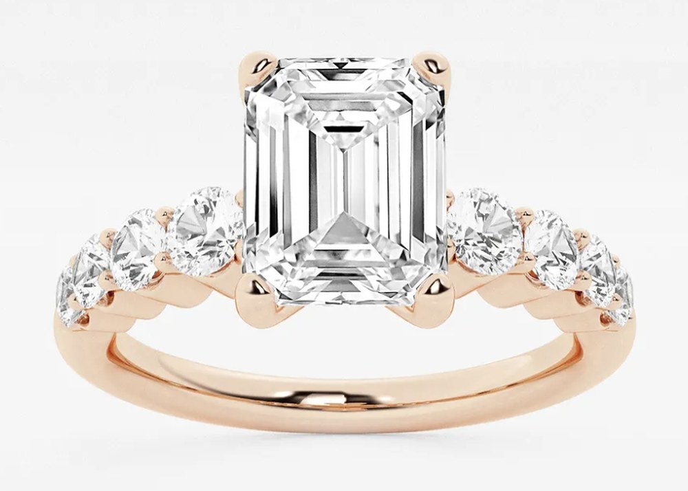 Emerald-cut engagement ring in rose gold, with round accent diamonds set along the band.