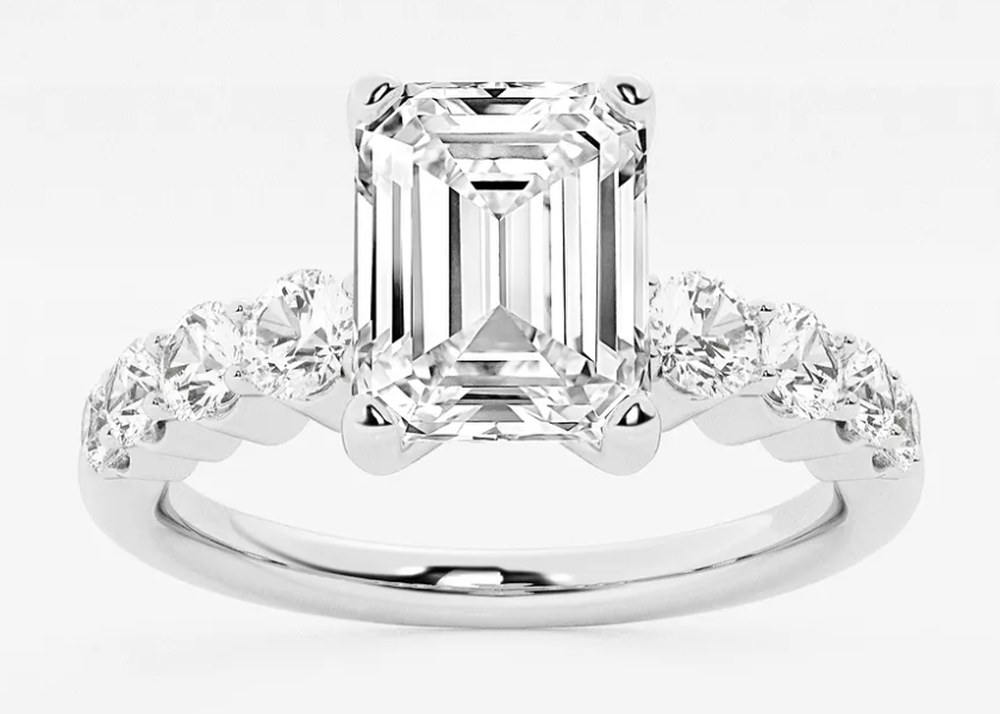 Emerald-cut engagement ring in white gold, with round accent diamonds set along the band.