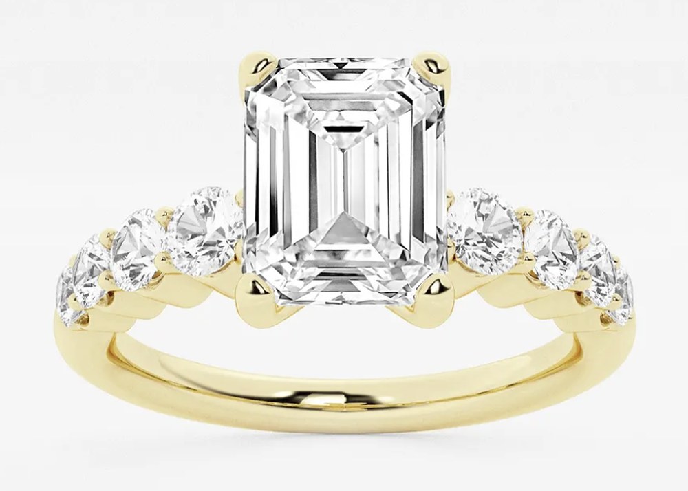 Emerald-cut engagement ring in yellow gold, with round accent diamonds set along the band.